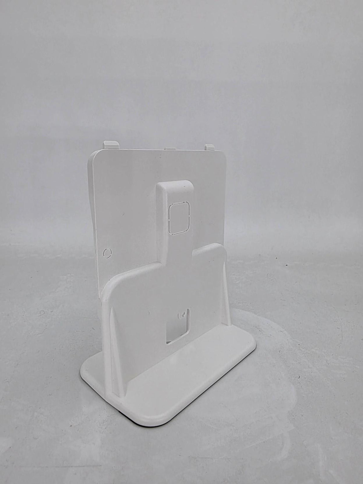 A white plastic tablet stand with a kickstand base and a vertical support arm, shown from a three-quarters angle on a light gray background.